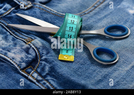 Jeans crotch and pocket, close up. Measure tape wound around metal scissors on jeans. Making clothes and design concept. Tailors tools on denim fabric, selective focus. Stock Photo