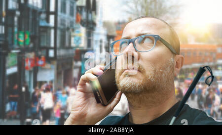 Young bling man using a smartphone white walking in the street with his cane. Empty copy space for Editor's text. Stock Photo