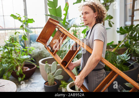 Young man as a gardener or florist with ladder in the garden center Stock Photo