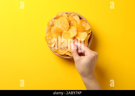 Hand holds potato chips on yellow background, space for text. Top view Stock Photo