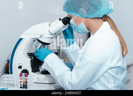 Young female scientist studying new substance or virus in microscope Stock Photo