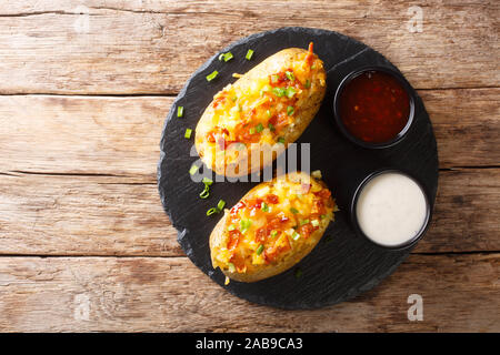 American food baked stuffed potatoes with cheddar cheese, green onions and bacon closeup on the table. Horizontal top view from above Stock Photo