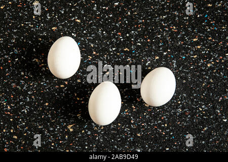 Still life, abstract arrangement with tree eggs lies on black spotted background. New life concept. Minimalistic white ovoid  flat lay, food art. Pop Stock Photo