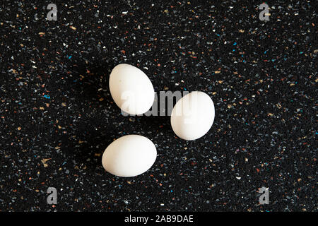Abstract arrangement with tree eggs lies on black mottled background. Minimalistic white eggs flat lay still life, food art. Pop art style. New life c Stock Photo