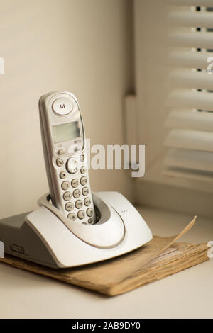 Telephone stands on the old phone book on a windowsill with shutters. Stock Photo
