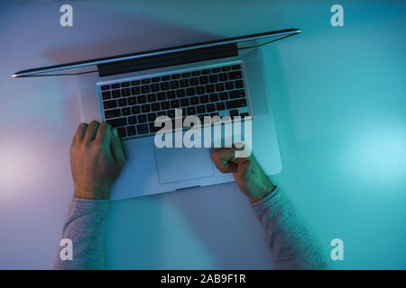 Man working night online silver laptop in the color light on a table night background. Top view. Stock Photo