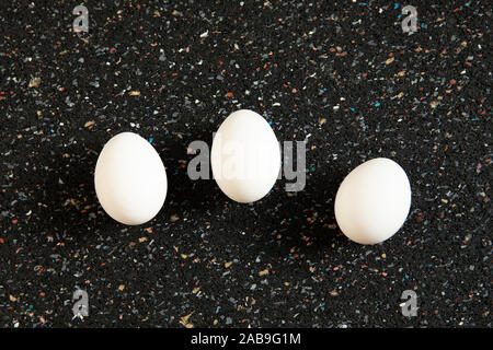 Still life, abstract arrangement with tree eggs lies on black spotted background. New life concept. Minimalistic white ovoid  flat lay, food art. Pop Stock Photo
