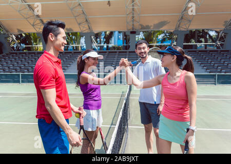Four young tennis players putting hands together before a doubles mixed match Stock Photo