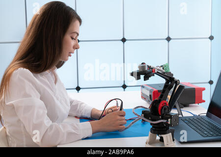 A young woman writes an algorithm for the robot arm. Science Research Laboratory for Robotic Arm Model. Computer Laboratory Stock Photo