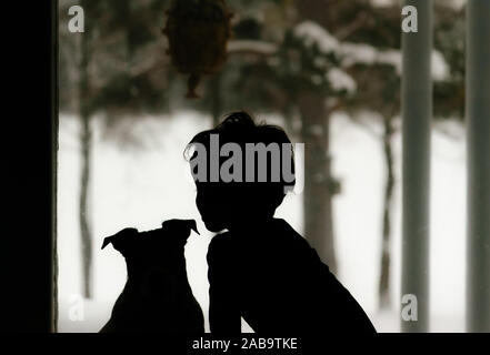 Silhouette of child and dog looking through window at winter landscape Stock Photo