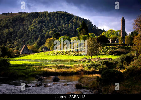 A river winds it's way past church and round tower at Glendalough Stock Photo