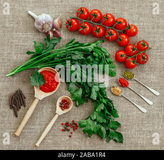 Food background. Flat lay. Cherry tomatoes, a bunch of parsley, black and red pepper, garlic and sauces adjika, pesto, mustard on burlap. Ingredients Stock Photo