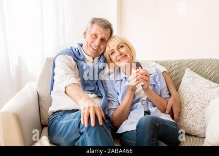 Happy mature couple sitting on sofa and embracing Stock Photo