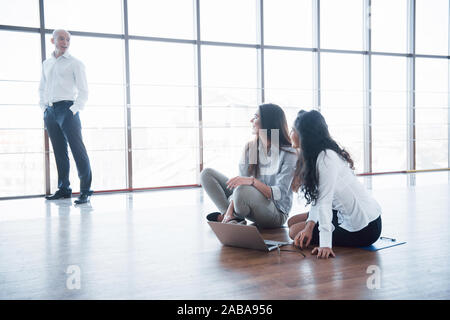Group of young business people are working together with laptop in the modern office. Freelancers sitting on the floor. Cooperation corporate Stock Photo