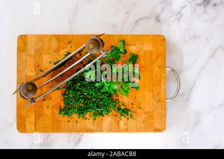 double bladed Mezzaluna, parsley whole and chopped, wooden board on marble Stock Photo