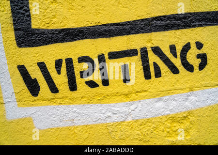 Fragment of graffiti drawing. Word “writing” in black on yellow old wall decorated with paint in street art style. Stock Photo
