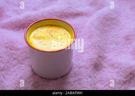 Mug of warm healthy drink turmeric golden milk on soft pink knitted background. Stock Photo