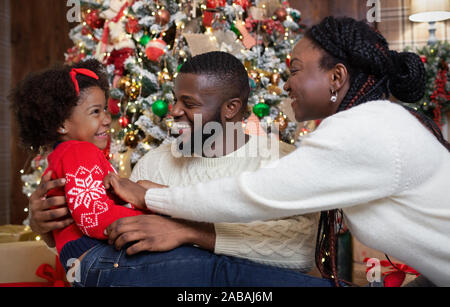 Joyful black parents tickling their little daughter, celebrating Christmas together Stock Photo