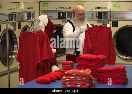 Santa wearing earphones getting ready for Christmas with all his red laundry Stock Photo