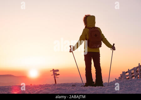 Skier girl stands with ski poles against sunset sky. Ski vacations or resort concept Stock Photo