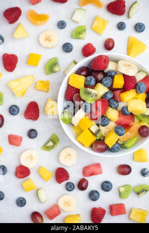 Bowl of cut fruit on a white background. Fruit includes raspberries, blueberries, banana, grapes, mango, pineapple, melon, kiwi and pear Stock Photo
