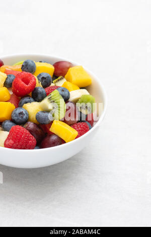 Bowl of cut fruit on a white background. Fruit includes raspberries, blueberries, banana, grapes, mango, pineapple, melon, kiwi and pear Stock Photo