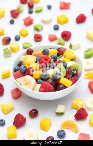 Bowl of cut fruit on a white background. Fruit includes raspberries, blueberries, banana, grapes, mango, pineapple, melon, kiwi and pear Stock Photo