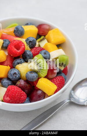 Bowl of cut fruit on a white background. Fruit includes raspberries, blueberries, banana, grapes, mango, pineapple, melon, kiwi and pear Stock Photo