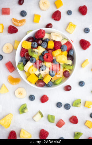 Bowl of cut fruit on a white background. Fruit includes raspberries, blueberries, banana, grapes, mango, pineapple, melon, kiwi and pear Stock Photo
