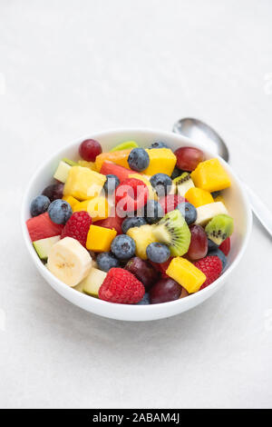 Bowl of cut fruit on a white background. Fruit includes raspberries, blueberries, banana, grapes, mango, pineapple, melon, kiwi and pear Stock Photo