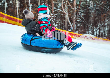 parent with kid sliding down by snowed hill with snowing tube Stock Photo