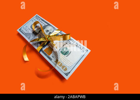 Stack of dollar banknotes with golden bow on orange background. Banner with copyspace Stock Photo