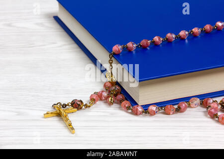 Rosary with pink colored grains lying on a book on a white wooden table Stock Photo