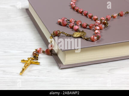 Rosary with pink colored grains lying on a book on a white wooden table Stock Photo