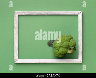 Fresh broccoli inside wooden frame on light green background Stock Photo