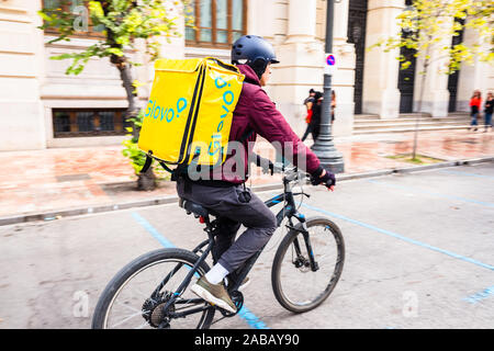 Valencia, Spain - November 24, 2019: Young rider man on a bike from the company Glovo circulating in the center of Valencia. Stock Photo