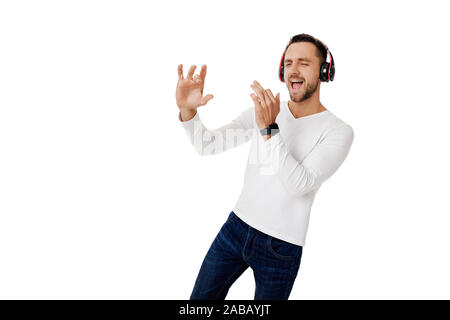 handsome young man in headphones listening to music and playing an imaginary musical trumpet isolated on white background. Stock Photo