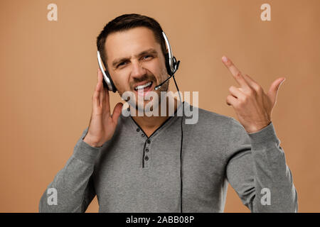 indignant unrestrained call center worker man isolated on beige background. Young angry employee telesales agent using headset. Stock Photo