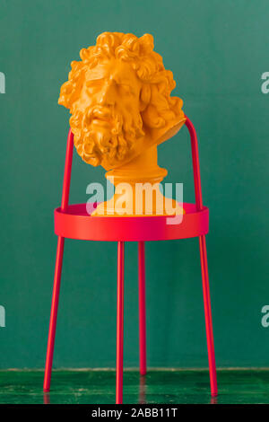 Color plaster head of ancient Greek sculpture on the red metal stand against green wall. Colorful plaser head concept Stock Photo