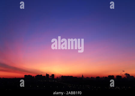 Sunrise over the city, scenic view. Pink-blue sky and cirrus clouds in soft colors above black silhouettes of high-rise buildings, colorful cityscape Stock Photo