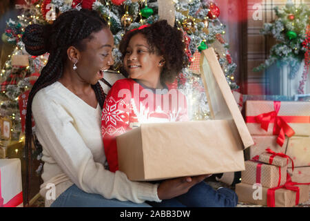 Happy african mother and daughter opening magical Christmas gift box Stock Photo
