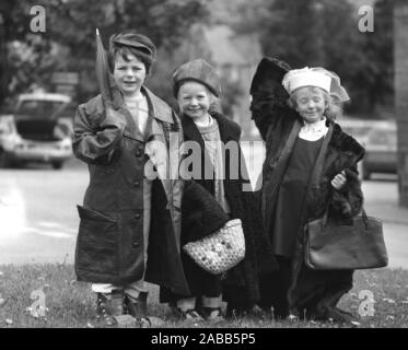 1980s, historical, three sweet little girls dressed up in some of a previous generation of adults clothes, hats and handbags, which are going to be on sale at a school jumble, including a 70s fashionable leather coat and a 1940s fur coat. Stock Photo