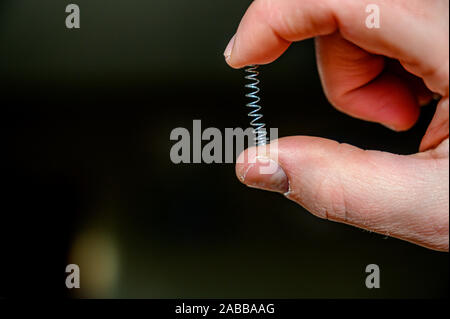 Caucasian hand compressing a metal spring between a thumb and finger ...