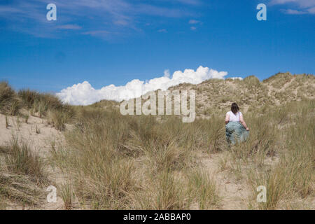 Woman walking in sand dunes on a windy day, Benar Beach, Barmouth, Gwynedd, Wales, UK Stock Photo