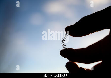 Silhouette of hand compressing a metal spring between a thumb and ...