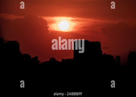 Red evil and menacing looking sky with the sun behind the clouds over skyscrapers and a the city of Hanoi, Vietnam Stock Photo