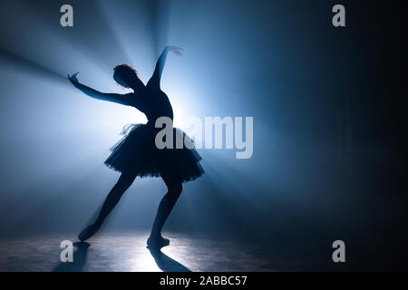 Ballerina in black tutu dress dancing on stage with magic blue light and smoke Stock Photo