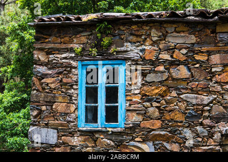 Close up of a window with blue trim and a rustic stone wall in the village of Cerdeira, Portugal Stock Photo