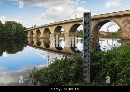 Water/flood level marker on the river Tyne at Hexham with Hexham road bridge spanning the river in Northumberland, UK. Stock Photo