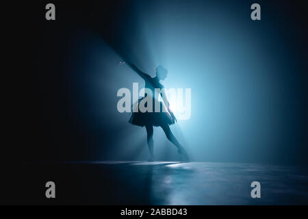 Ballerina in black tutu dress dancing on stage with magic blue light and smoke Stock Photo